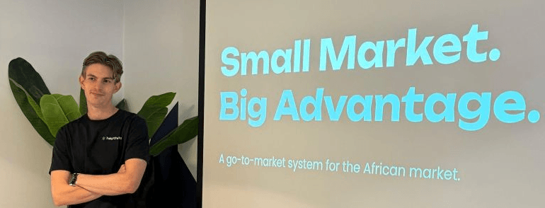 Marlon Dickerson standing with his arms folded beside a projected slide that reads "Small Market. Big Advantage. A go-to-market system for the African market."